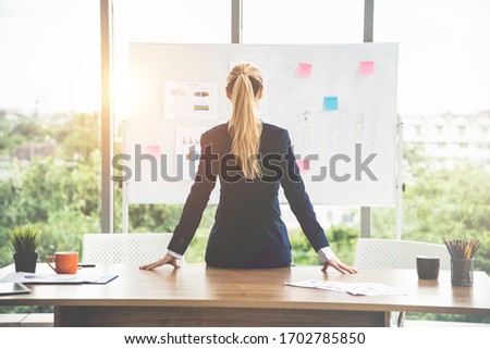 Businesswoman sit and turn your back on the table and looking at future business plans on a board