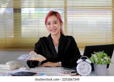 Businesswoman sits at her desk at work, holding cash money in dollar banknotes. - Shutterstock ID 2251867349