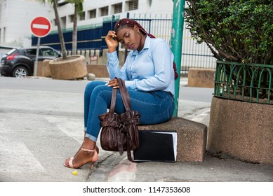 Businesswoman Sitting Alone On The Street With Her Documents And Bag, Feeling Worried And Stressed After A Day Of Searching For Work In The City.