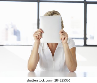 Businesswoman Sitting At Desk In Office With Face Hidden Behind Digital Tablet - Powered by Shutterstock