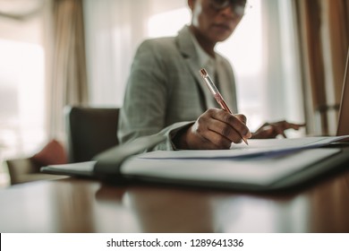 Businesswoman Sitting At Hotel Room Desk Writing On Document. Focus On Female Hand Making Notes While Working At Hotel Room Desk.