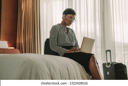 Businesswoman Sitting On Bed Using Laptop. African Woman On Business Trip Working In Hotel Room.