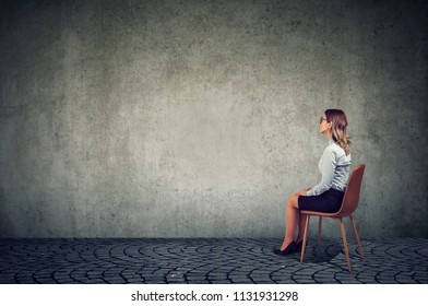 Businesswoman sitting on a chair in front of a wall and thinking 
