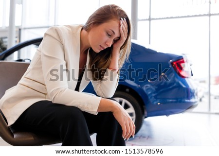 Businesswoman sitting on a chair holding his head from the problems on the background of the car. Confiscation of the car for tax evasion