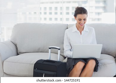 Businesswoman sitting on the couch using laptop beside her suitcase