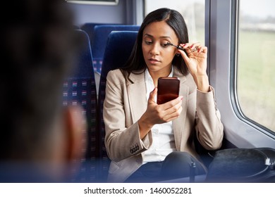 Businesswoman Sitting In Train Commuting To Work Putting On Make Up