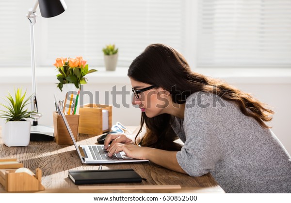 Businesswoman Sitting In Wrong Posture Working On\
Laptop On Wooden Office\
Desk