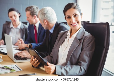 Geschäftsfrau lächelt Kamera an und Geschäftsleute interagieren im Konferenzraum während der Besprechung