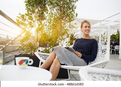 Businesswoman Is Smiling For Someone, While Is Sitting With Portable Touch Pad In Restaurant In The Fresh Air. Cheerful Female Entrepreneur Is Resting After Reading Electronic Book Via Digital Tablet