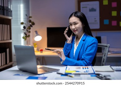 Businesswoman smiling while talking on phone and pointing at laptop during night shift at office - Powered by Shutterstock