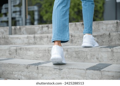 A businesswoman in sneakers conquers the city stairs, symbolizing her determined path. Each step reflects her unwavering progress towards success, highlighting her professional growth. step up - Powered by Shutterstock