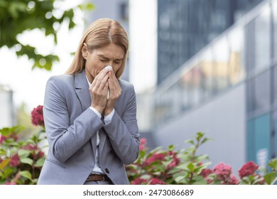 Businesswoman sneezing outdoors surrounded by plants, possibly due to allergies or cold symptoms. Professional attire suggests work environment. - Powered by Shutterstock