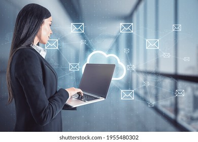 Businesswoman standing and holding a laptop with cloud holo symbol and message icons in the background, business communication and social media concept - Powered by Shutterstock