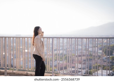 Businesswoman is standing on a rooftop, talking on her phone and enjoying the view of the city and mountains in the background during a sunny day - Powered by Shutterstock