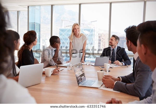 Businesswoman Stands To Address Meeting Around\
Board Table