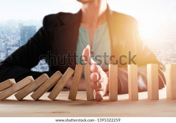 Businesswoman stops a chain fall\
like domino game. Concept of preventing crisis and failure in\
business.