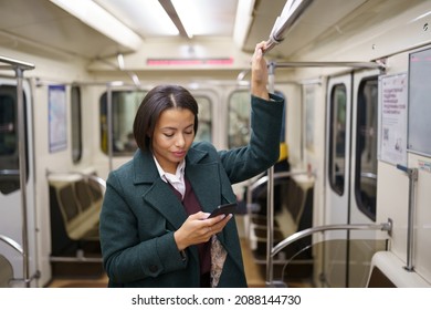 Businesswoman In Subway Carriage Using Smartphone To Send Business Email Or Text With Family. Young African American Female Travel By Public Transport Standing In Empty Underground Wagon Late At Night