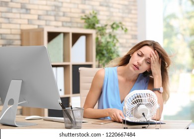 Businesswoman suffering from heat in front of small fan at workplace