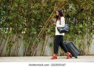 Businesswoman With Suitacase Walking Down Street And Checking Map On Smartphone