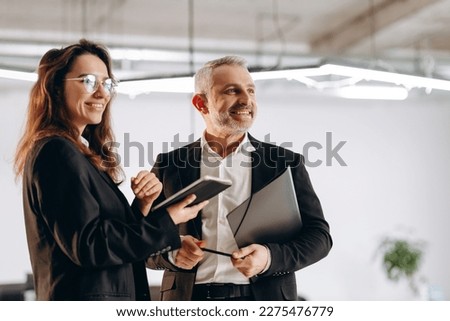 Businesswoman with tablet and businessman with folder. Smiling coworkers standing in office together