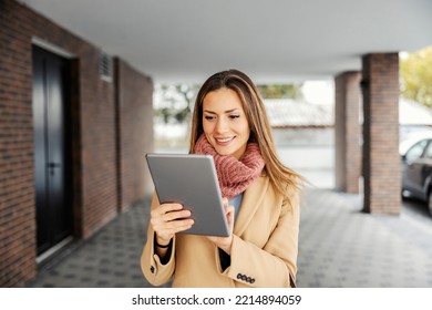A businesswoman with a tablet outdoors. A happy businesswoman in warm clothes standing outdoors and using the tablet for web research.