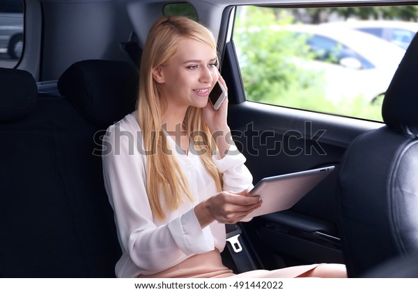 Businesswoman\
with tablet speaking by cellphone in a\
car
