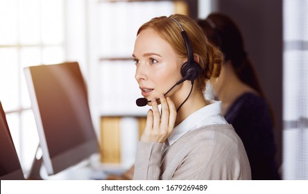 Businesswoman talking by headset in sunny office. Call center and diverse people group in business - Shutterstock ID 1679269489