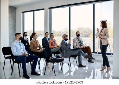 Businesswoman Talking To Group Of Her Colleagues During Education Event In Board Room. All Of Them Are Wearing Protective Face Masks Due To Coronavirus Pandemic.