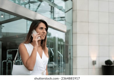 Businesswoman talking on mobile phone near office building. Female entrepreneur during business conversation on cellphone. Woman manager making phone call before meeting - Powered by Shutterstock