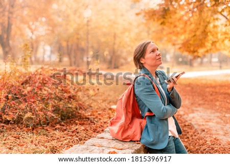 Businesswoman talking on mobile phone in autumn park, holding smartphone in front of her face, selective focus
