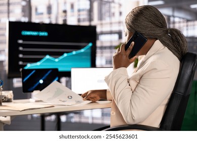 Businesswoman in telephone call with shareholders, analyzing market trends and data in office. Entrepreneur talking on phone with partners to develop trading strategies and algorithms - Powered by Shutterstock