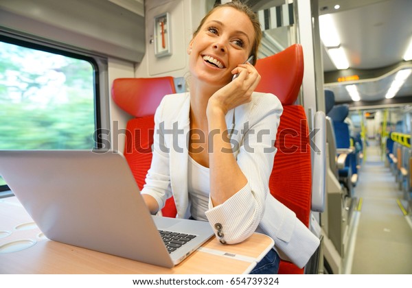 Businesswoman in train working on laptop and\
talking on phone