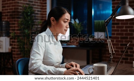 Businesswoman transcribing information from laptop to notepad, doing tasks for team project in office overnight. Worker working late at night, writing down data from computer screen