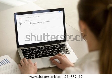 Businesswoman typing e-mail on laptop at office desk, composing professional email letter using business etiquette, writing e message to corporate client online, focus on screen, close up rear view