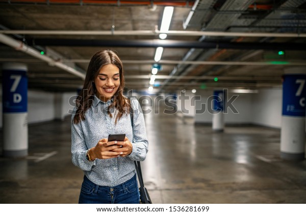 Businesswoman in\
underground garage. Elegant woman using smartphone in parking\
garage. Fashionable young woman texting on smartphone.\
Businesswoman in a parking\
garage