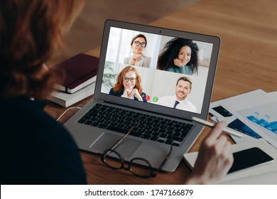 Businesswoman uses laptop application for communication with several people, has vitrual conference, works freelance from home, sits at desktop, surrounded with paper documents. Online negotiations