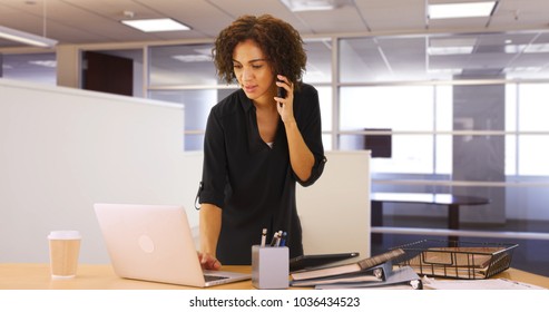 Businesswoman using laptop computer in office while listening on smartphone device