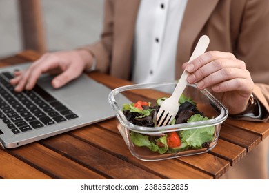Businesswoman using laptop during lunch at wooden table, closeup - Powered by Shutterstock