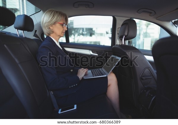 Businesswoman using\
laptop while traveling in car\
