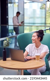 Businesswoman Using Laptop Working At Table In Breakout Seating Area Of Office Building