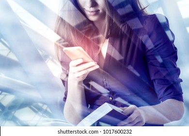 Businesswoman using smartphone with digital business interface and holding book on abstract city background. Online education, technology and media concept. Double exposure  - Powered by Shutterstock