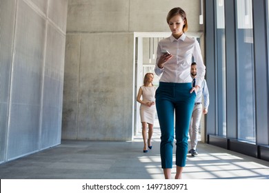 Businesswoman Using Smartphone While Walking In Office Hall