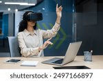 Businesswoman using virtual reality headset in modern office, interacting with digital interface. Young woman immersed in VR technology, exploring virtual workspace, innovation in business