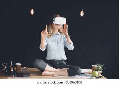businesswoman in virtual reality headset sitting in lotus pose on table in office - Powered by Shutterstock