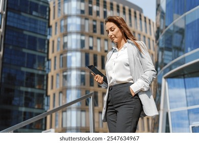 Businesswoman Walking Down Stairs While Checking Smartphone in Modern Urban Setting With Glass Buildings - Powered by Shutterstock