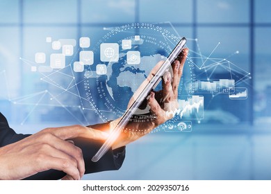 Businesswoman wearing formal suit is touching a tablet with digital interface with globe, cloud data, padlock, coin icons. Blurred office in background. Concept of international business and network