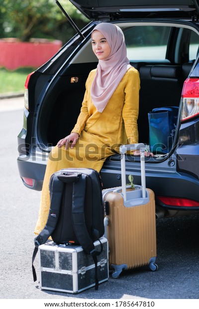 Businesswoman wearing hijab on a business travel \
with suitcase sitting in car\
trunk.