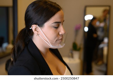 Businesswoman is wearing a transparent face mask in an office setting, demonstrating safety measures during the coronavirus pandemic - Powered by Shutterstock