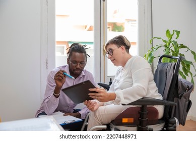 a businesswoman in a wheelchair with a disability looking at the digital tablet with her multiethnic business partner discussing the business plan - Powered by Shutterstock