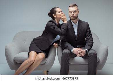 businesswoman whispering something on colleague's ear while sitting on chairs - Powered by Shutterstock